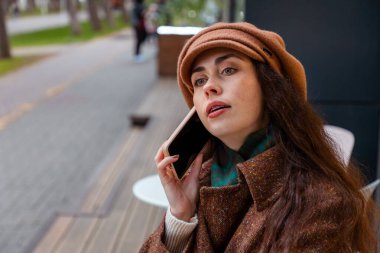 Genç beyaz kadın portresi, sonbahar şehrinde bir haftasonu gezintisinden zevk alır. Telefonunu tutar ve mesajlarını kontrol eder. Mevsimlik cazibesine hayran kalır.