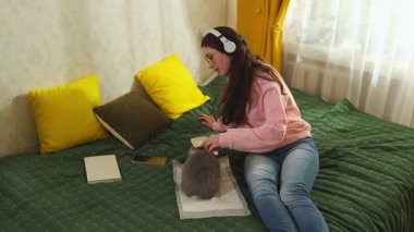 Beyaz tenli genç yatakta oturuyor, tavşan tutuyor ve tarağını tımar etmek için kullanıyor. Hayvan bakımı, ev hayatı ve evcil hayvan sevgisi kavramı. Geniş açı.