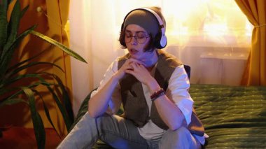 Modern gençlik kıyafetleri içinde gözlüklü düşünceli bir kadın laptopta yataktan, online kariyer büyümesi konsepti, serbest çalışma projeleri ve ev ofisinden çalışıyor.