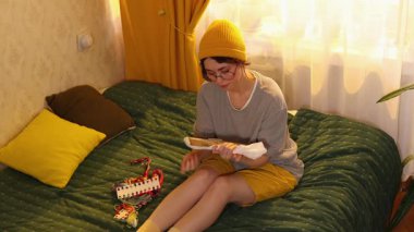 Güzel, genç, beyaz bir kadın evde yatakta çember nakış işliyor. Çapraz dikiş çalışması yapıyor ve yaratıcı gevşetici eğlencelerden zevk alıyor.