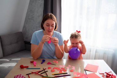 Kafkasyalı genç bir anne ve küçük tatlı kızının balonları şişirip tatil için dekorasyon yaptığı bir fotoğraf. Aile masaya oturur ve şenlikli dekorasyonlar yapar..