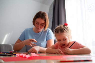 Genç anaokulu öğretmeninin düşük açılı görüntüsü bir kıza tatil için nasıl kartpostal çizileceğini öğretir. Beyaz kadın ve küçük kız birlikte vakit geçiriyorlar..