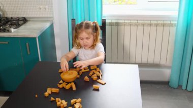 Anaokulundaki beyaz kız, parlak bir sınıftaki bir masada tahta blok oyununa odaklanmış. Etkileşimli faaliyetler bilişsel büyüme ve beceri geliştirmeyi teşvik eder