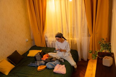 Beyaz bir kadın gün batımında odasında giysilerini katlıyor. O, düzenli depolamaya odaklanıyor. Ev organizasyonu ve günlük rutin konsept. Üst görünüm.