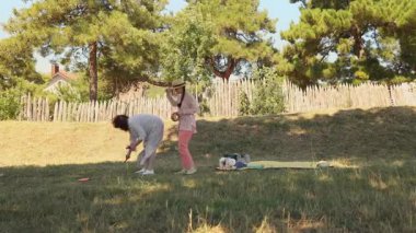 Annesi onu cesaretlendirirken küçük kızı yüzüklerini fırlatıyor. Parkta piknik, açık havada aile eğlencesi ve yaz tatili. Geniş açı. Rüzgarlı hava