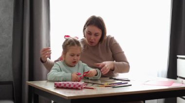 Kafkasyalı genç bir kadın ve küçük tatlı bir kız anneler günü kartlarını kesip masada oturuyorlar. Okul öncesi çocukların eğitimi..