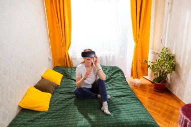 Genç bir kadın oyun oynamak için sanal gerçeklik gözlüğü kullanıyor. Üst manzara, geniş açı.