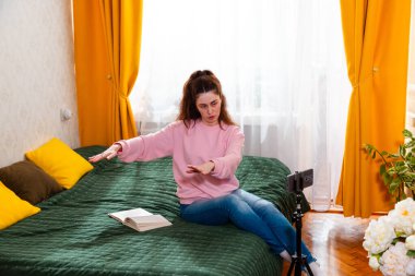 Genç beyaz kadın yatağında oturuyor, sosyal medya takipçileri için bir video kaydediyor, yaşam tarzı ipuçlarını paylaşıyor. Geniş açı.