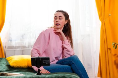 Şık bir içerik yaratıcısı yatağında otururken sosyal medya için ilgi çekici bir video kaydediyor. Orta çekim.