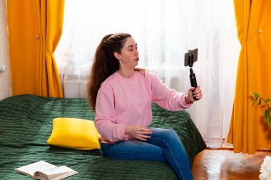 Sıcak bir yatakta oturup online markalaşmayı tartışırken dijital içerik oluşturan şık bir etki yaratıcının orta pozu