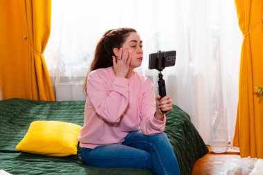 Yatağında oturan ve yüksek değerli içerikler yaratan çevrimiçi girişimci, bir sosyal medya videosu çekiyor. Sosyal medya kavramı.