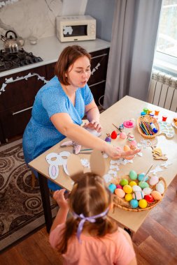 Çocukların renkli süslemelerle dolu rahat bir mutfakta Paskalya zanaatı yarattıkları neşeli bir sahne..