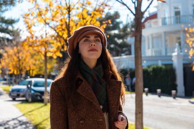 Güneşli bir şehirde sonbahar caddesinde şapkası ve paltosu olan güzel beyaz bir kadının resmi. Psikoloji kavramı ve pozitif ruh hali.