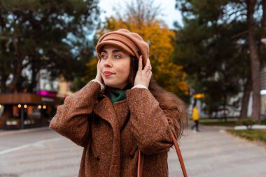 Bej ceketli ve bereli genç bir bayanla sonbahar şehri yürüyüşü sahnesi. Barışçıl bir solo gezisi sırasında en sevdiği şarkı listesini dinliyor.