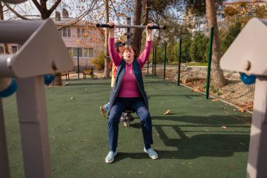 Şehir parkındaki bir spor salonunda yaşlı, beyaz bir kadın antrenman yapıyor. Spor, sağlık ve aktif kıdemli yaşam tarzı konsepti.