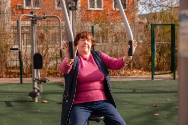 Yaşlı kadın dışarıda spor aletleri üzerinde güç egzersizi yapıyor. Aktif yaşam tarzı ve kıdemli sağlık