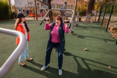 Yaşlı kadın, hastalık sonrası iyileşme sürecinin bir parçası olarak antrenör gözetiminde egzersiz yapıyor. Yapılandırılmış spor rutini önleme ve sağlıklı yaşlanmayı destekler