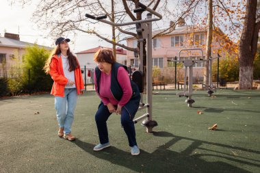 Üst düzey Kafkasyalı kadın halka açık bir parkta profesyonel bir eğitmenle rehabilitasyon egzersizleri yapıyor. Fiziksel aktivite hastalıktan sonra iyileşmeyi destekler ve genel olarak sağlığı güçlendirir.