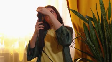 Kıvırcık esmer saçlı bir kadın, saç kurutma makinesini rahat dairesinde saç kurutmak için kullanıyor, günlük bakım ve kişisel bakım kavramı. Orta çekim.