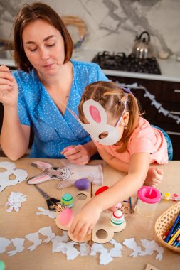 Genç Kafkasyalı anne ve küçük kızı evde Paskalya yumurtası ve el yapımı süslemeler hazırlayıp bahar tatilini ve geleneksel aile değerlerini neşeyle kutluyorlar. Dikey.