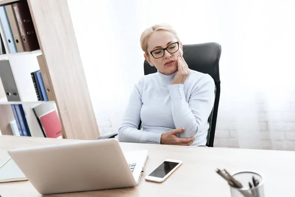 A woman sits at a desk and feels a toothache. — Stock Photo, Image