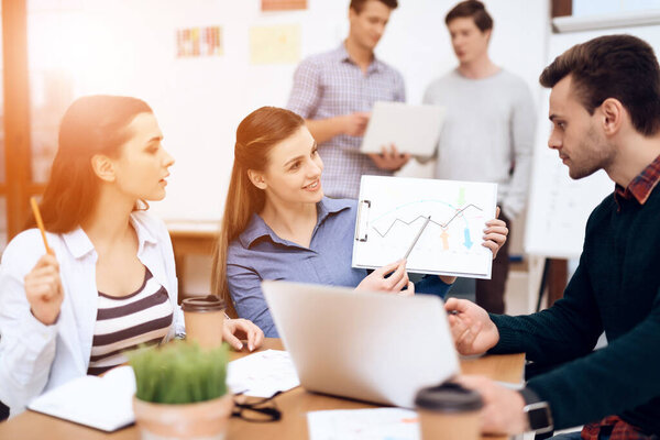 The girl at the table shows colleagues a graph.