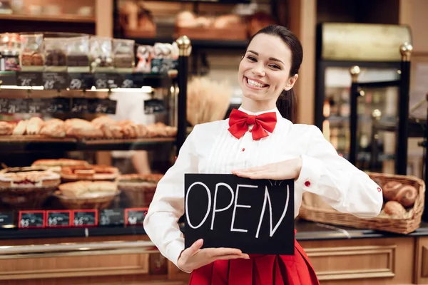 Mladá žena s otevřeným nápisem stojící v pekárně. — Stock fotografie
