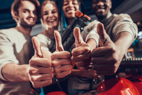 Group of young friends giving thumbs up in arcade.