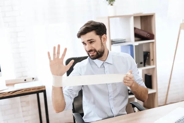 Um homem com barba senta-se à mesa e ataduras mão. — Fotografia de Stock