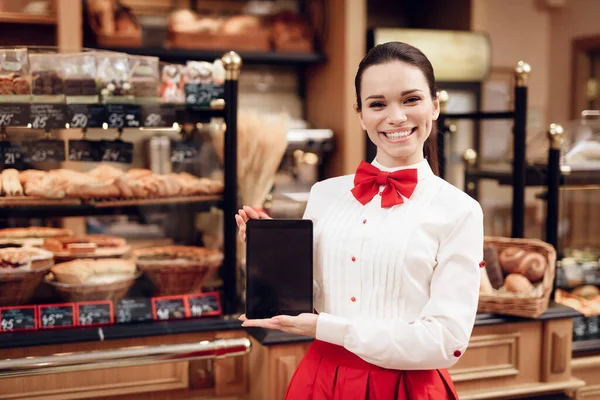 Jonge glimlachende vrouw met behulp van tablet in de moderne bakkerij. — Stockfoto