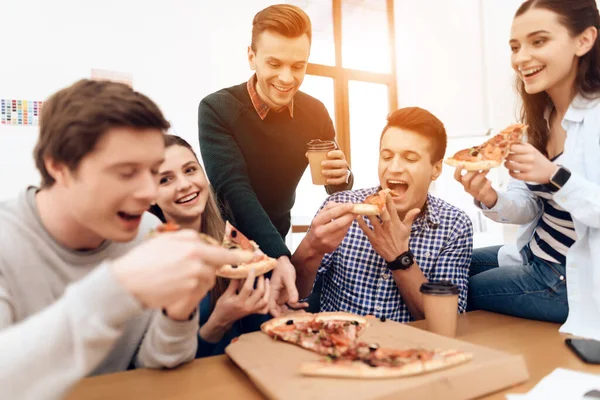 Люди сидят и едят пиццу в офисе вместе. — стоковое фото