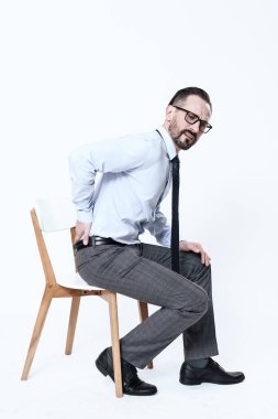 Gömlekli bir adam sandalyeye oturur ve sırtı ağrır.