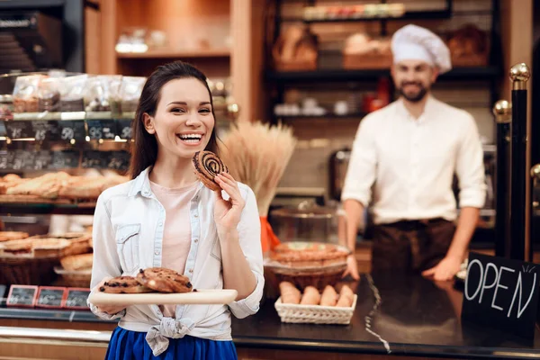 Jonge glimlachende vrouw eet broodjes in de moderne bakkerij. — Stockfoto