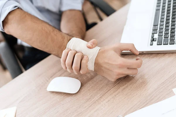 A male injured hand lies on table at a computer. — Stock Photo, Image