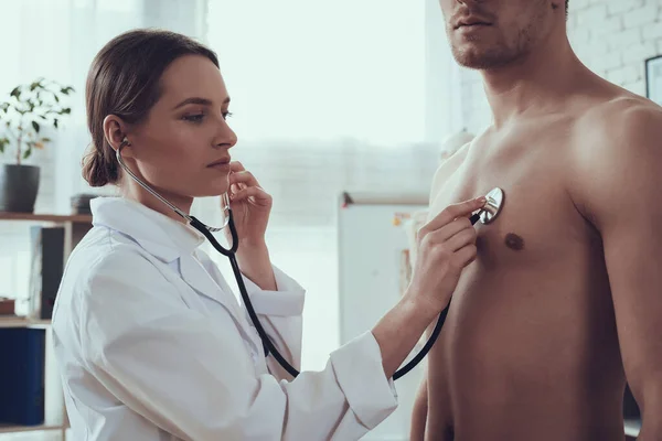 Doctor listens to a male athlete with stethoscope.