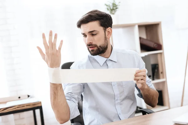 Un hombre se sienta a la mesa y le vendan la mano.. — Foto de Stock