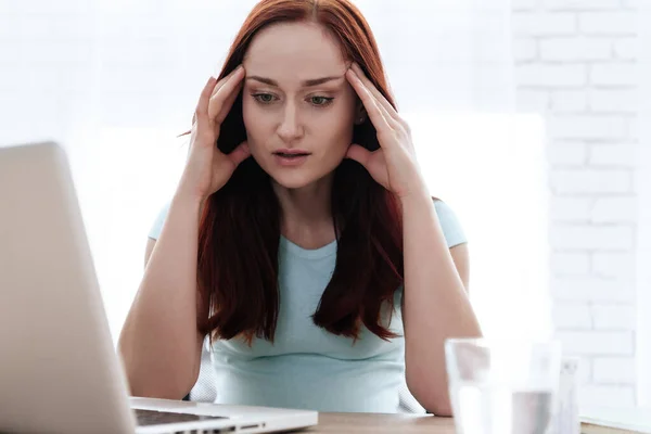 Girl sitting at a laptop and holds hands on head. — Stock Photo, Image