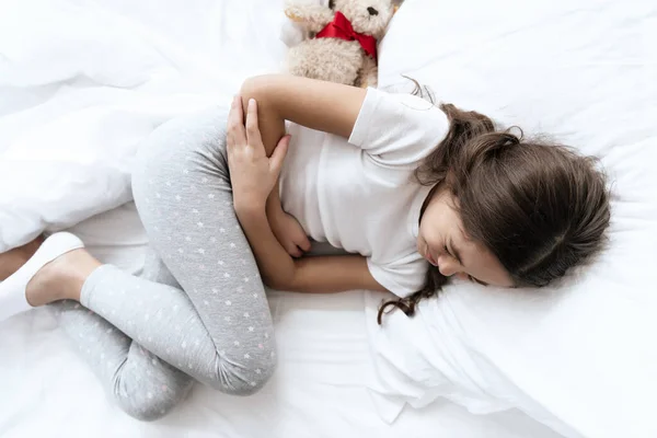 Niña sostiene su estómago mientras está acostada en la cama. — Foto de Stock