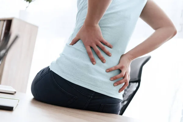 Kvinna sitter på ett kontor och lägger två händer på ryggen — Stockfoto