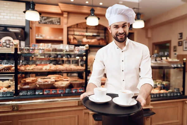Mladý vousatý muž v bílé čepici stojící v pekárně. — Stock fotografie