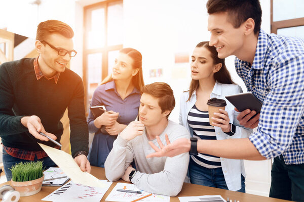 People stand around boss who is sitting.