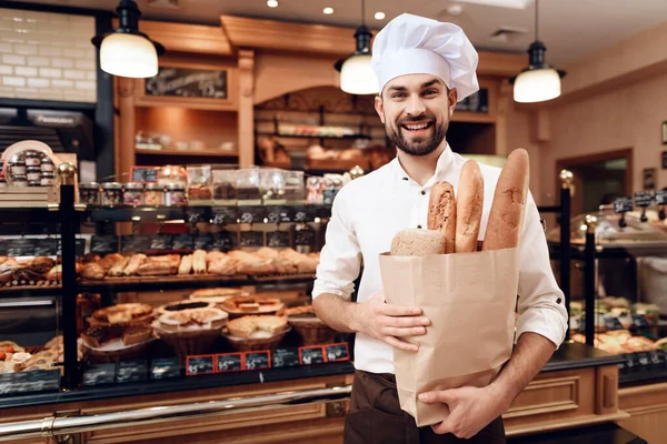 Jonge man met baard in witte pet staand in de bakkerij. — Stockfoto