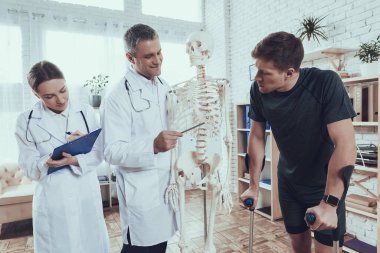 Doctors are showing skeleton to injured sportsman. clipart
