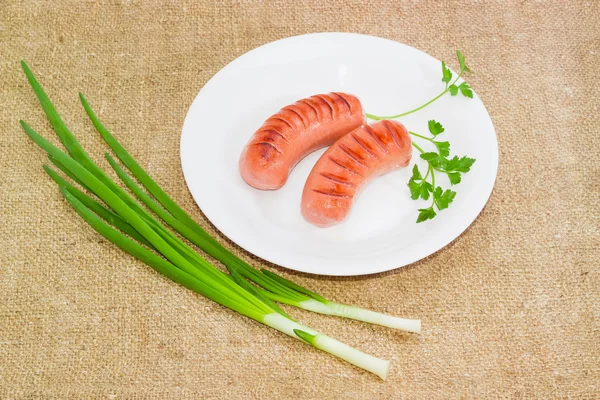 Grilled sausages, sprig of parsley on white dish, green onion — Stock Photo, Image