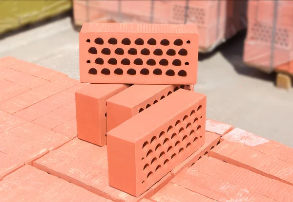 Several red perforated bricks against of pallets of bricks close — Stock Photo, Image