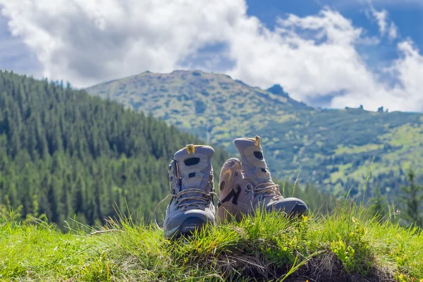 Trekking schoenen op onscherpe achtergrond van beboste bergen en s — Stockfoto