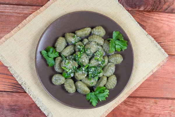 Pişmiş patates gnocchi, ıspanak çeşnili beyaz sos ve kırsal masada kahverengi tabakta doğranmış yeşillikler.