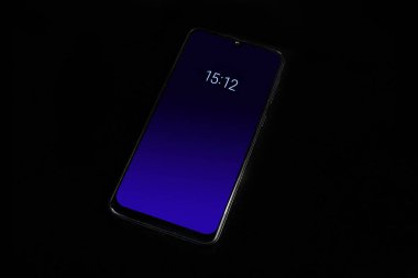 Karanlık yüzeyde dijital saat görüntüsü olan koyu mavi kilit ekranlı modern akıllı telefon