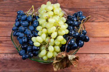 Kırsal masada meyveler için yeşil cam vazoda olgunlaşmış mavi üzümler ve beyaz çekirdeksiz sultana üzümleri.