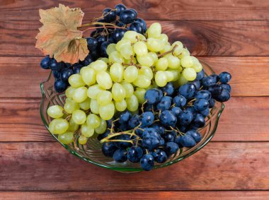 Kırsal masada meyveler için yeşil cam vazoda olgunlaşmış mavi üzümler ve beyaz çekirdeksiz sultana üzümleri.